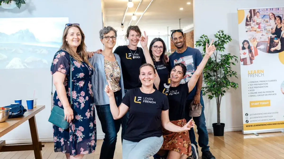 A group of seven smiling people poses together in a bright loft-style space with wooden at Learn French Canada, Vancouver